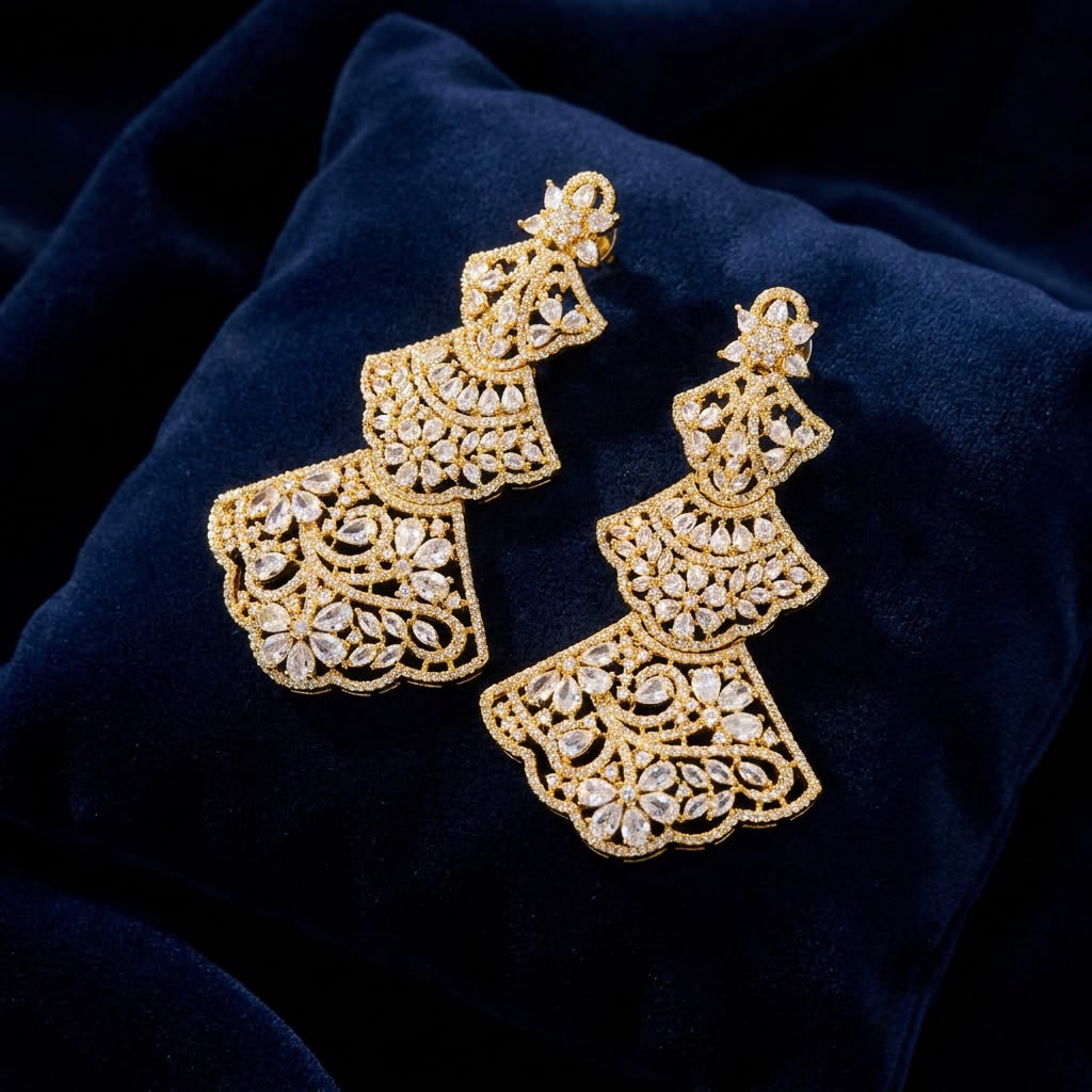 Close-up of elegant gold-toned statement earrings with detailed filigree patterns and marquise-cut crystals, resting on a luxurious dark blue velvet cushion.