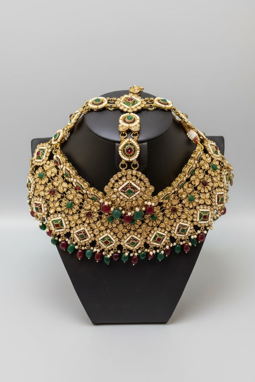 Decorative gold necklace with gemstones on a black stand, held by a hand.