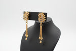 Detailed view of rose gold peacock drop earrings with three dangling chain strands and gold bead finishes on a stand.