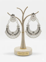 Detailed view of silver-based crescent-style earrings featuring intricate metal cut-outs and shimmering accents.