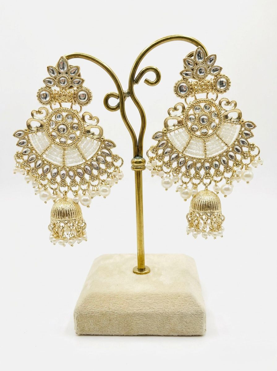 Dull gold ethnic earrings displayed on a stand, showing the intricate kundan-style work and bottom jhumka drop.