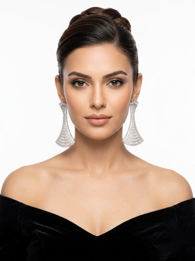 Elegant silver statement chandelier earrings with a geometric flared fan design, fully paved in brilliant white crystals, worn by a model in a black off-the-shoulder dress.