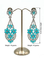 A pair of ethereal teal blossom statement earrings on a display stand.