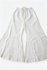 A flat-lay view of a pair of ethereal white sharara pants, showcasing delicate paisley motifs and intricate Bakhiya embroidery detail, set against a clean white background.