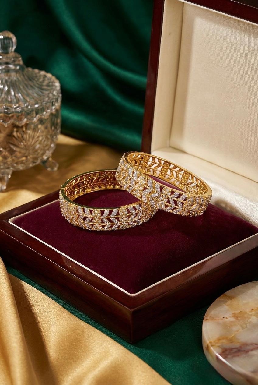 A pair of premium dual-tone American Diamond bangles featuring an intricate gold floral lattice and silver leaf vine design, elegantly displayed inside a maroon velvet luxury jewelry box.