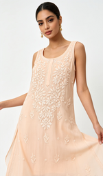 A woman modeling a sleeveless peach-colored dress with intricate white floral embroidery on the front, set against a plain light gray background.
