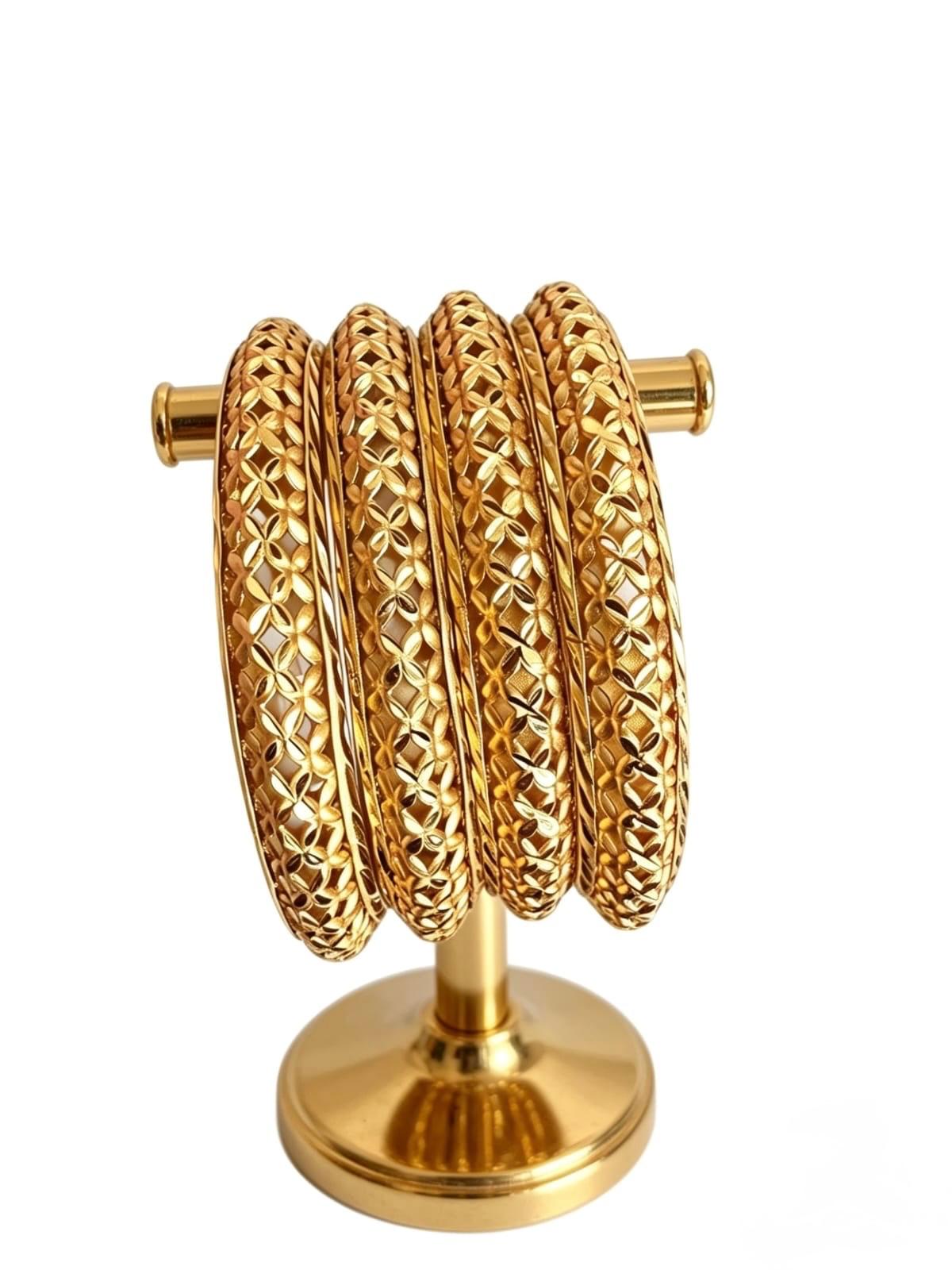 A set of four micro-gold plated copper bangles featuring an intricate fan-pattern lattice cutwork design, displayed on a gold-toned jewelry stand against a white background.