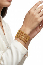 A lifestyle view of a person wearing a set of four micro-gold plated copper bangles with an intricate fan-pattern design, styled with a white silk outfit.