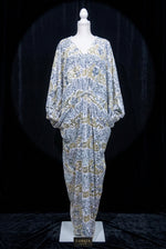 Famaza Couture white velvet kaftan gown on white mannequin, silver sequins and gold floral embroidery, floor-length V-neck formal wear.