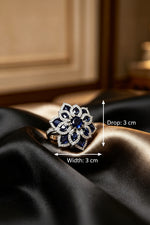 Studio render of the Famaza Couture sapphire and American diamond floral cocktail ring resting on luxurious black and gold satin-silk fabric.