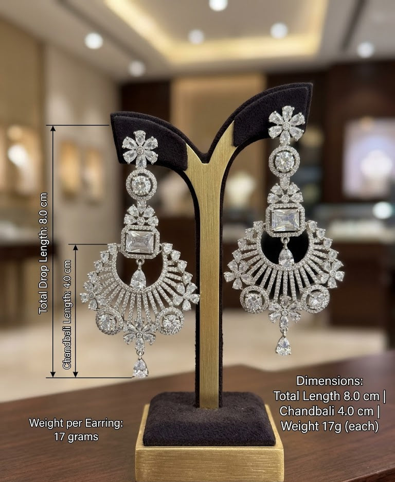 A pair of elegant silver-toned chandelier earrings featuring intricate floral designs and sparkling clear cubic zirconia stones displayed on a posh stand.