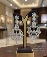 A pair of elegant silver-toned chandelier earrings featuring intricate floral designs and sparkling clear cubic zirconia stones displayed on a posh stand.
