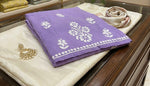 Folded purple trouser with white floral pattern on a beige surface, surrounded by jewellery.