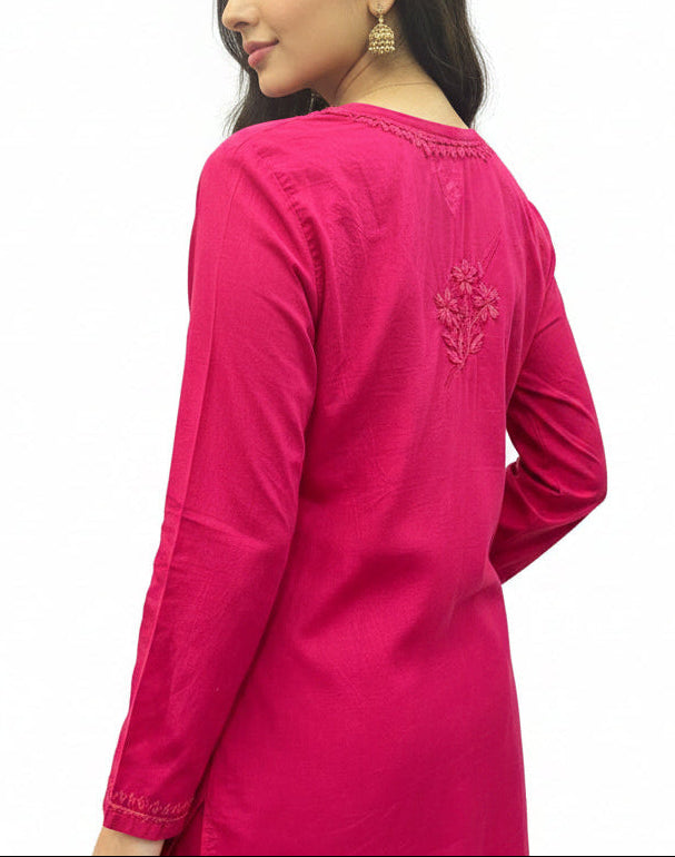 Back view of a model wearing a fuchsia pink cotton short kurti featuring intricate embroidery along the upper back neckline and a floral motif centered on the upper back.