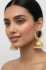 Gold earrings with pearl accents on a stand against a textured white background