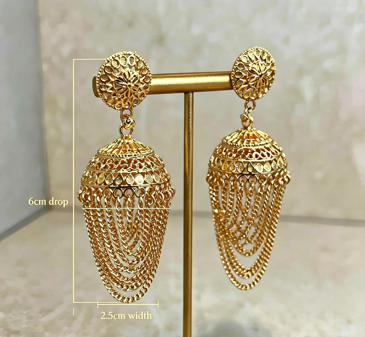 Gold-plated filigree jhumka earrings on gold display stand with dimensions — 6cm drop, 2.5cm width — intricate floral stud top, openwork dome design, cascading layered chain fringe, premium Pakistani bridal jewellry.