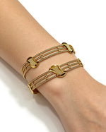 A pair of premium gold-tone interlocking design bangles worn on a wrist, featuring a delicate lattice structure and a high-shine, non-openable solid profile by Famaza Couture.