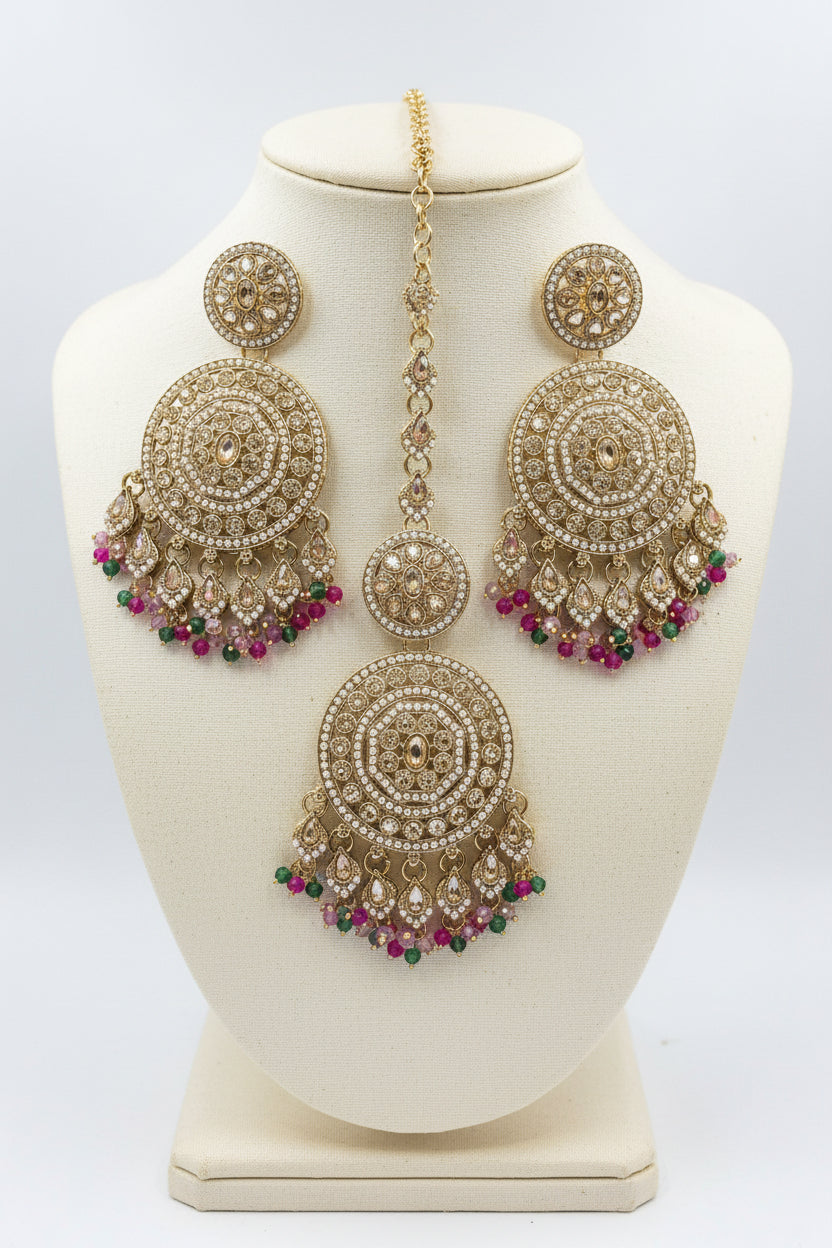 Gold-toned Indian maang tikka with matching stud earrings, decorated with clear crystals and colourful dangling beads in pink, green, yellow, and blue, displayed on a black background with a clear card.