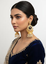 Gold and black earrings with gemstones held in a hand, with a blurred background of more jewellery.