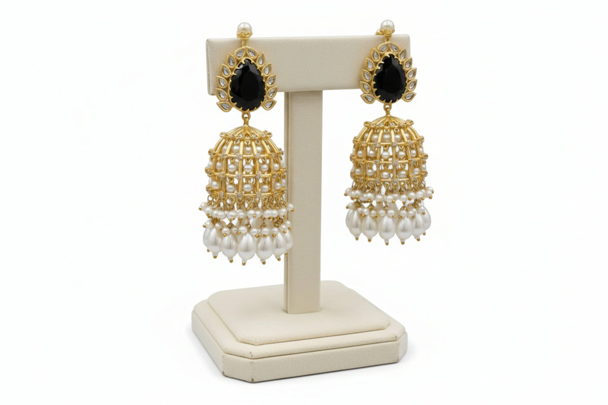 Gold and black earrings with pearl drops on a white stand against a pure white background