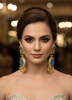 Gold and blue gemstone earrings on a white fur background