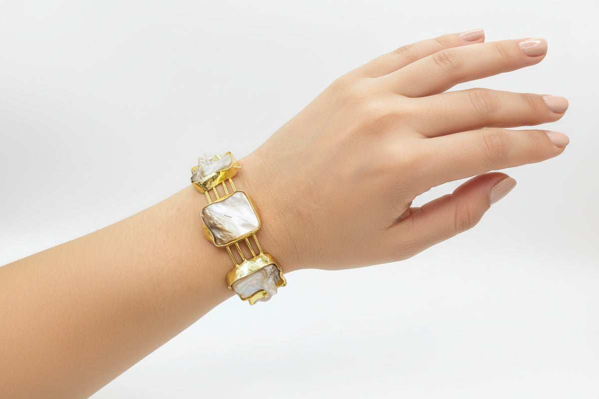 Gold bracelet with large mother of pearl stones on a wrist against a white background