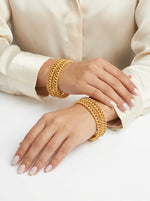 Gold bracelets on a person's wrist against a white background
