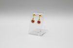 Gold earrings with red stones on a dark textured surface