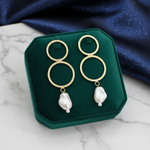 Gold hoop earrings with pearl drops on a black card against a white background