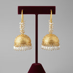 Gold hoop earrings with intricate designs on a stand against a textured white background