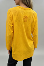 Rear view of a woman wearing a vibrant yellow cotton short kurti featuring a delicate floral motif embroidered on the back yoke and a square hem line, paired with dark trousers in an indoor boutique setting.