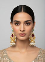 Gold and red gemstone earrings held by a hand with a blurred background