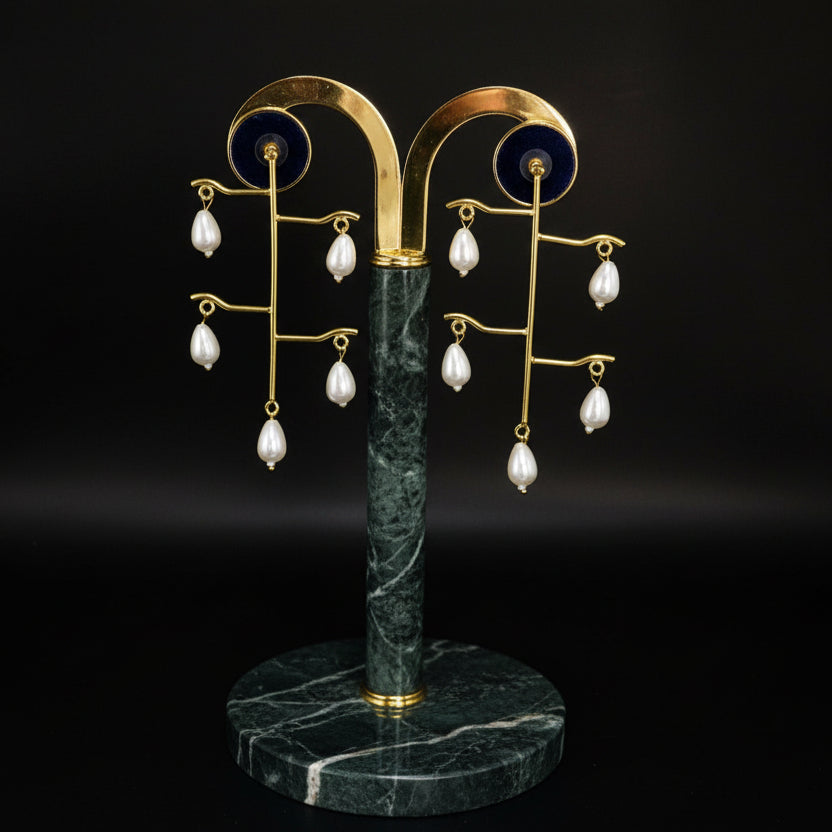 Woman wearing gold earrings with pearl-like beads on a gray background