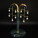 Woman wearing gold earrings with pearl-like beads on a gray background