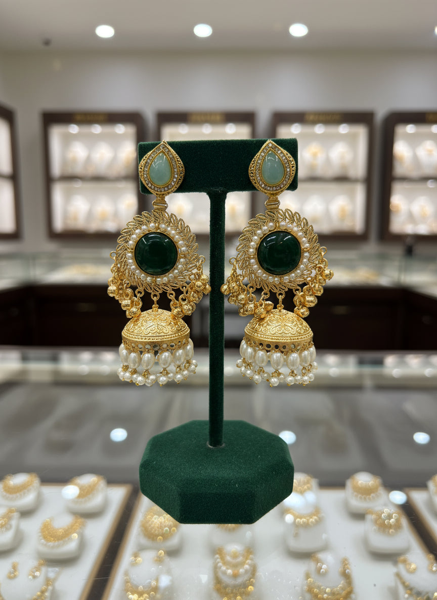 Gold and green earrings held in a hand with a blurred background