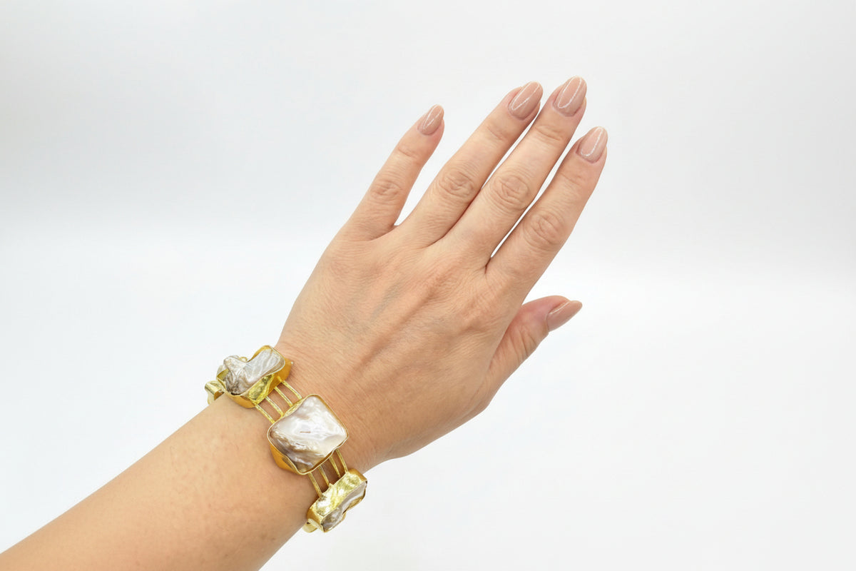 Hand wearing a gold bracelet with large stones on a white background