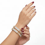 Hand wearing two gold bracelets on a white background