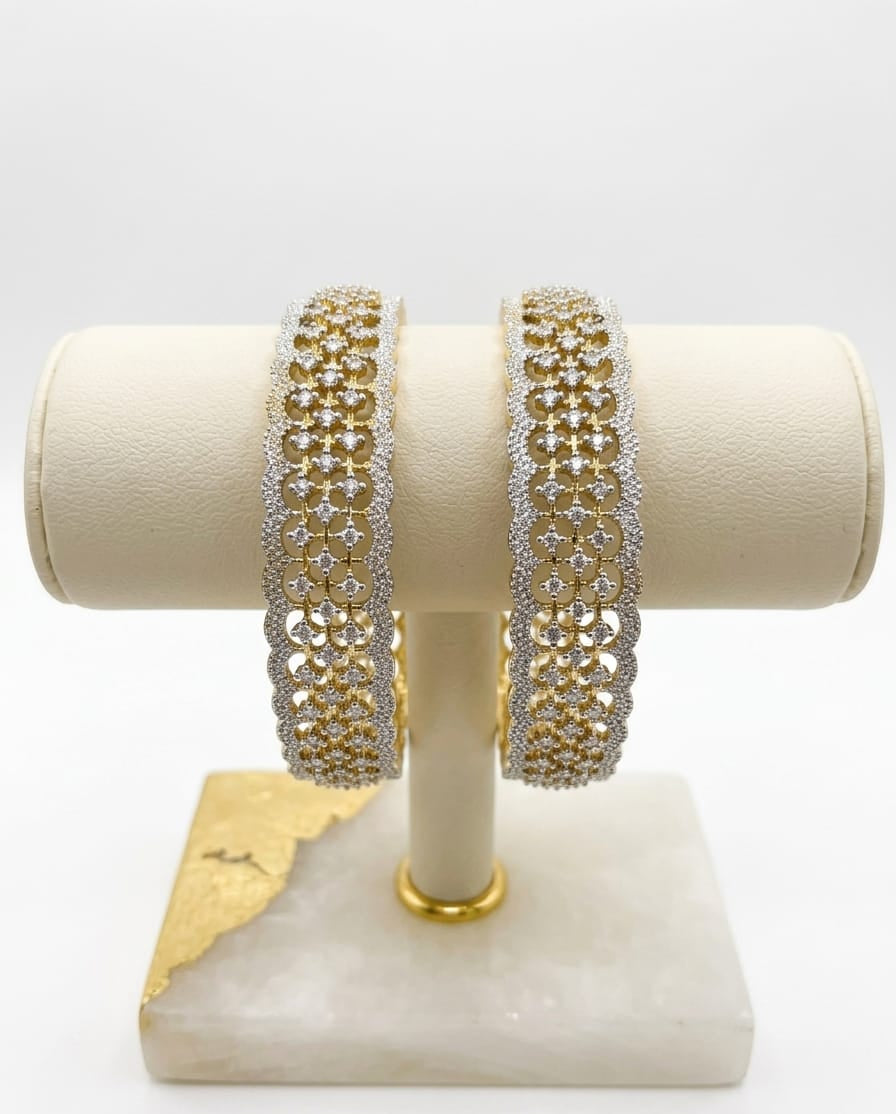 Close-up of premium dual-tone American Diamond bangles with a gold and silver lattice design, displayed on a creamy-white cushioned jewelry stand.