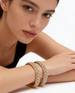 Model wearing a pair of handcrafted gold-plated American Diamond bangles featuring an intricate leaf and vine motif with marquise-cut stones.