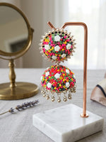 Handcrafted multicolor beaded floral jhumka earring with white rose motifs hanging on a copper and marble display stand