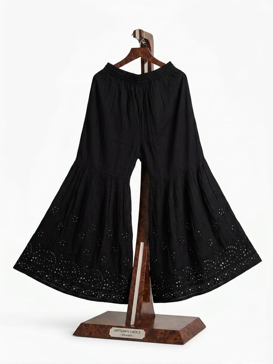 Front view of a black cotton tiered gharara featuring intricate antique silver Kaamdani and Bakhiya threadwork, displayed on a wooden stand.