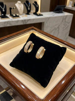 High-detail shot of geometric rose gold hoops on a brass stand, highlighting the shimmering stone-encrusted surface.
