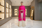Hot pink shawl with floral patterns draped over a mannequin next to a black handbag on a small table against a marble wall.