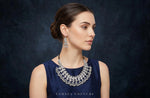 A woman in profile wearing a dark navy sleeveless top and a large silver statement necklace with matching drop earrings, set against a dark textured studio background. The brand name 'FAMAZA COUTURE' is printed at the bottom of the image.