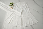 White wide-leg flared pants with a textured, eyelet-like woven pattern, laid flat on a light wood floor.