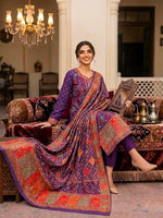 A woman in a posh, palace-like interior wears a deep imperial purple silk kurta set with multicolored Kanni embroidery and zari work, seated on a luxurious sofa with a detailed dupatta, to showcase the premium dress.