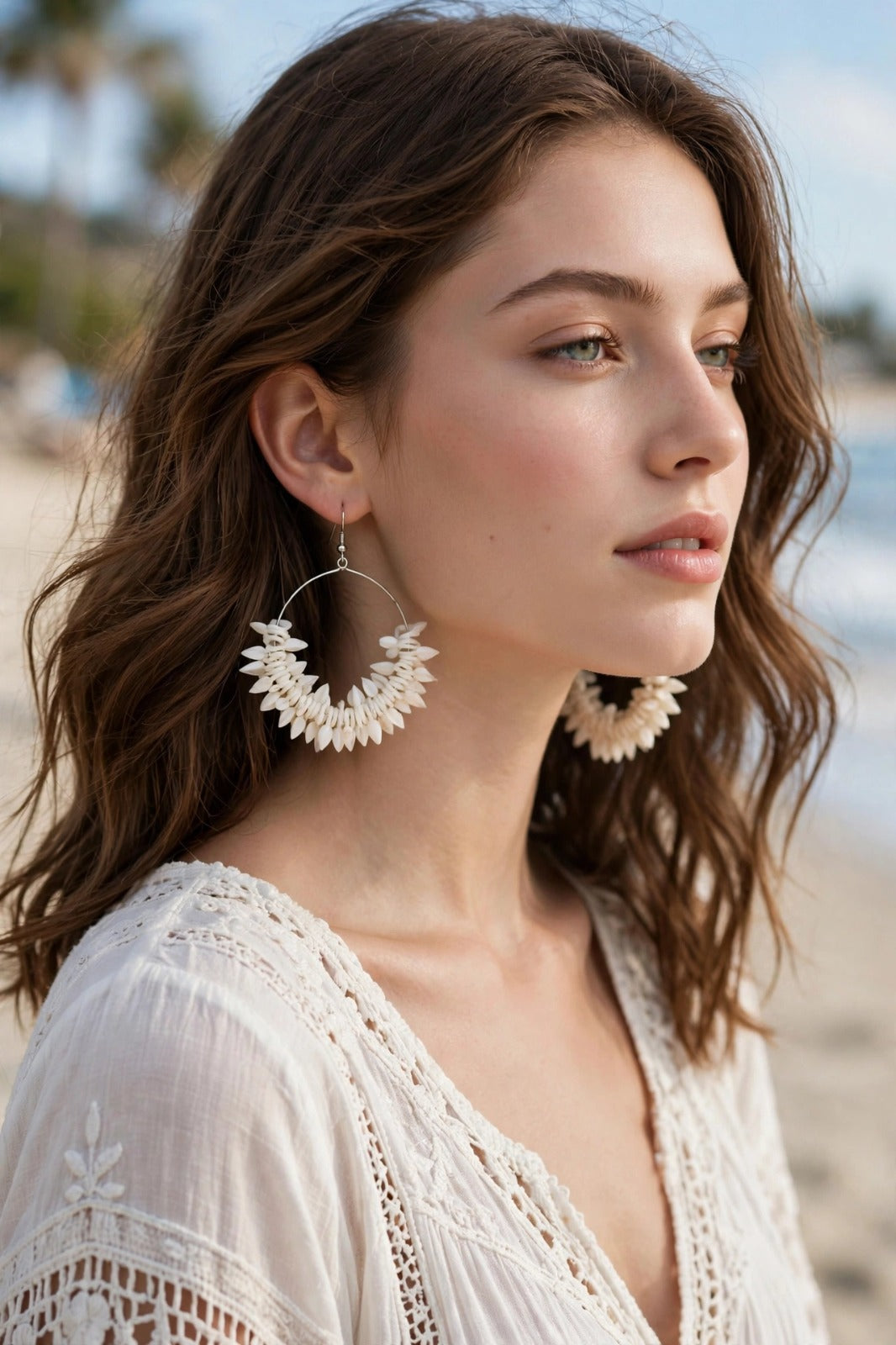Woman wearing ivory white natural shell petal cluster hoop earrings with silver-toned wire frame, beach background — Famaza Couture.