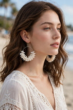 Woman wearing ivory white natural shell petal cluster hoop earrings with silver-toned wire frame, beach background — Famaza Couture.