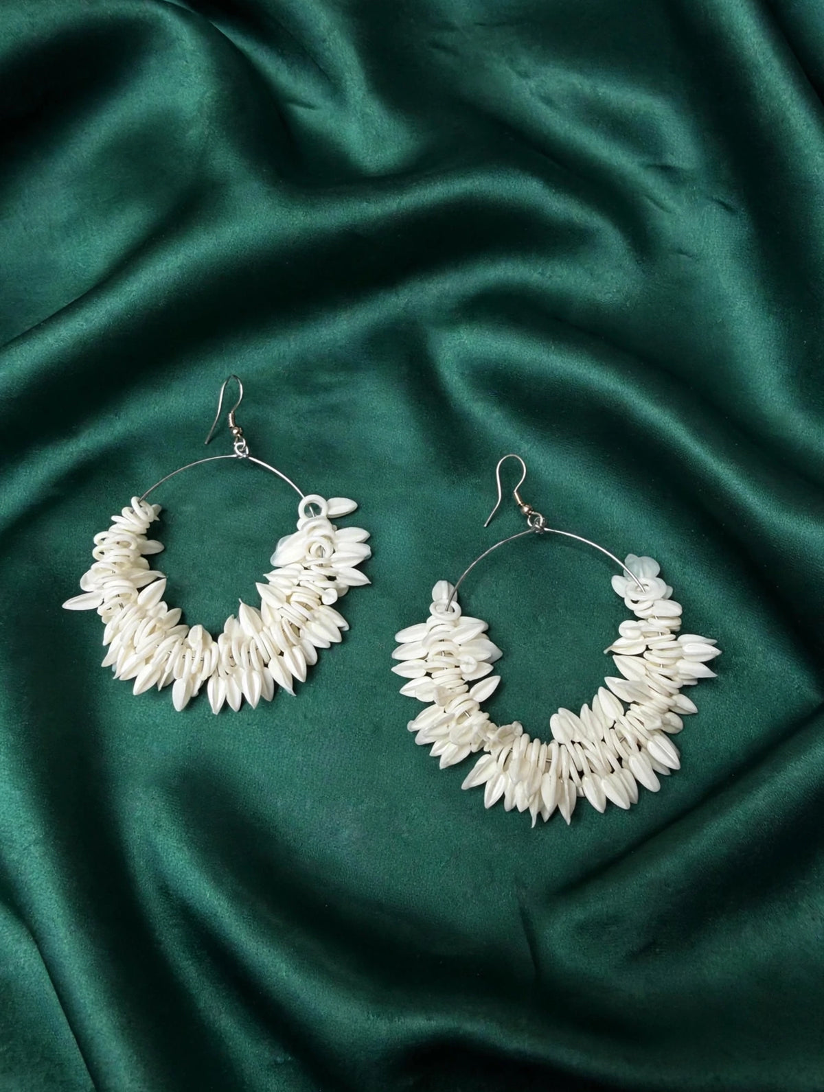 Pair of ivory shell petal cluster hoop earrings with carved rose detail on rich emerald green silk satin background — Famaza Couture.