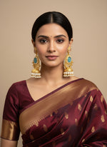 Gold and pearl earrings with blue gemstones held by a hand against a blurred background.